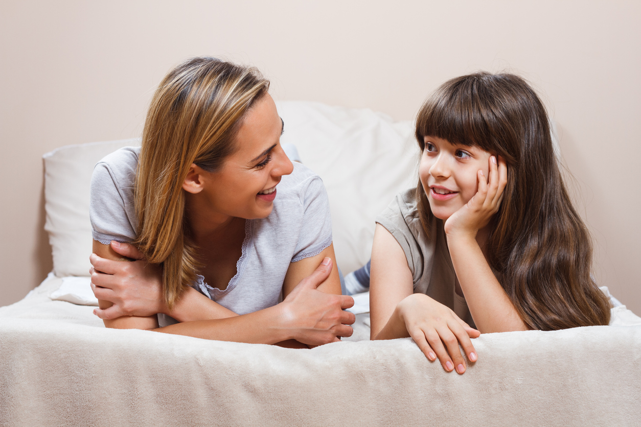 Mother and daughter chatting while lying on a bed.